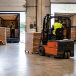Cross-docking: qué es y cómo funciona Operación de cross-docking en un almacén logístico con carretilla elevadora, palés y camiones en los muelles de carga.